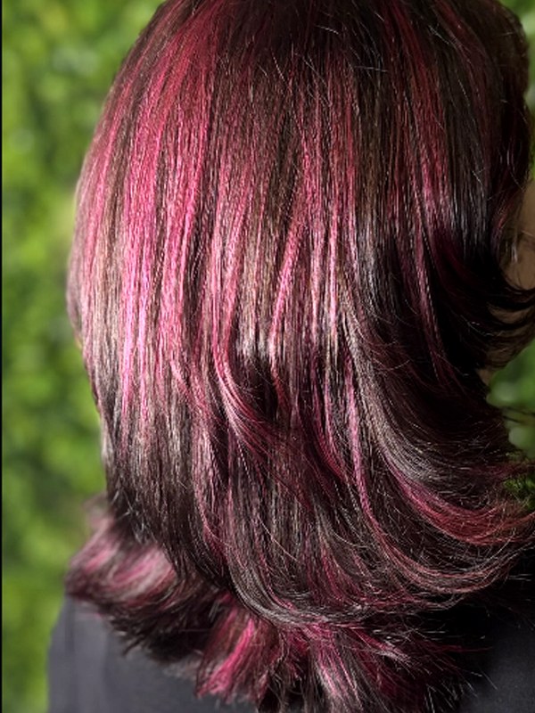 Schulterlanges dunkles Haar mit magenta Highlights, gestuft und glänzend gestylt